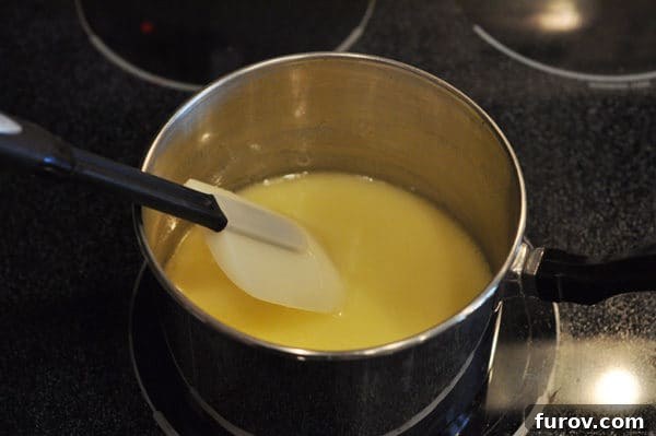 A heatproof spatula gently stirs a smooth, melted butter and sugar mixture in a saucepan, ensuring thorough dissolution without scorching.