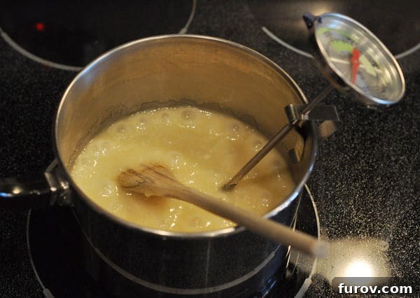 A candy thermometer is securely clipped to the side of a saucepan, accurately measuring the temperature of the boiling butter and sugar mixture, which is being stirred by a wooden spoon.