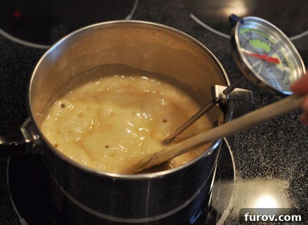 The bubbling butter mixture in the saucepan continues to cook, stirred by a wooden spoon, with a candy thermometer showing its rising temperature.