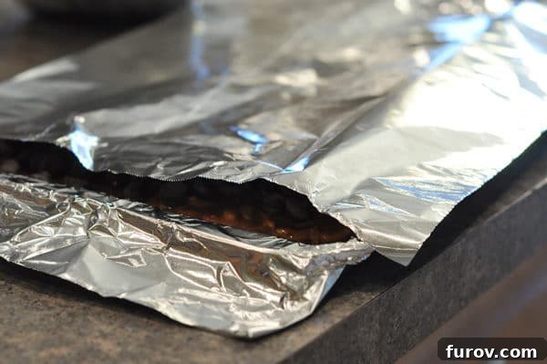 A cookie sheet containing chocolate chip-covered almond roca is tented with aluminum foil to help melt the chocolate evenly.