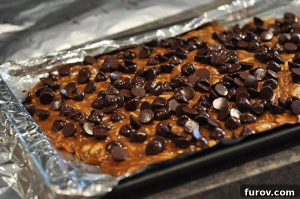 The chocolate chips have melted into a smooth, glossy layer over the almond roca on the foil-lined cookie sheet, looking utterly delicious.