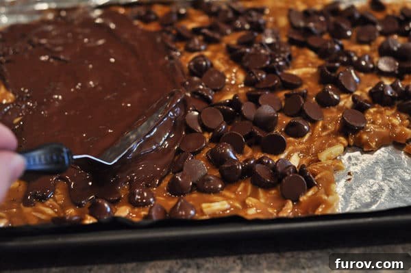 An offset spatula smoothly spreads melted chocolate over the chocolate chip-covered almond roca, creating an even, tempting layer.