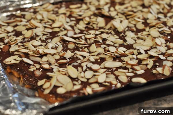 Sliced almonds are sprinkled generously over the chocolate-covered almond roca, which is resting on a foil-lined cookie sheet to cool and set.