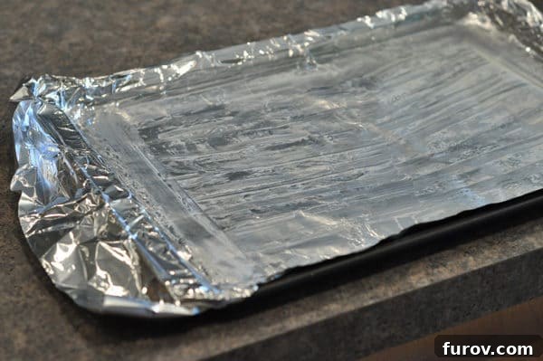 A baking sheet is perfectly lined with aluminum foil and lightly buttered, ready for the hot toffee mixture.