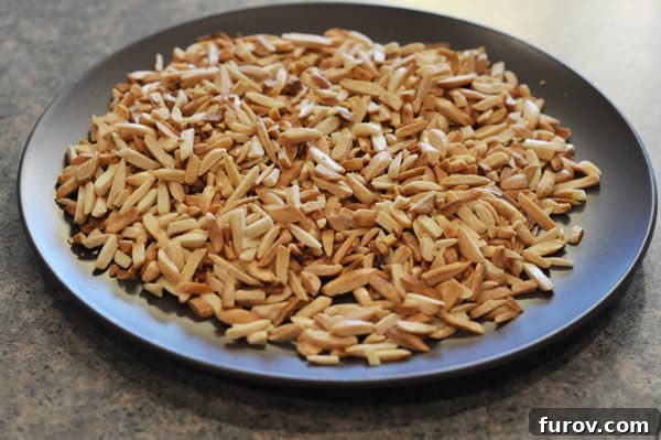A dark plate holds a generous pile of perfectly toasted slivered almond slices, ready for the almond roca recipe.