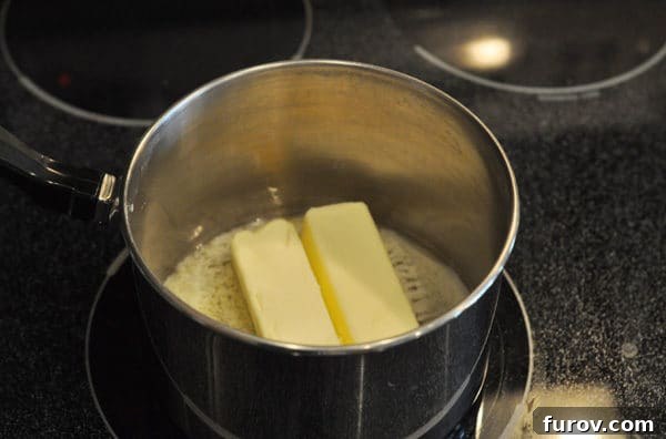 Two sticks of butter are gently melting in a saucepan on the stove over medium-low heat, creating a smooth base for the toffee.