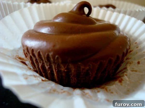 Peanut Butter Pods 3 A single, perfectly crafted chocolate peanut butter cup nestled in a crisp white muffin liner, showcasing its smooth, solid appearance.