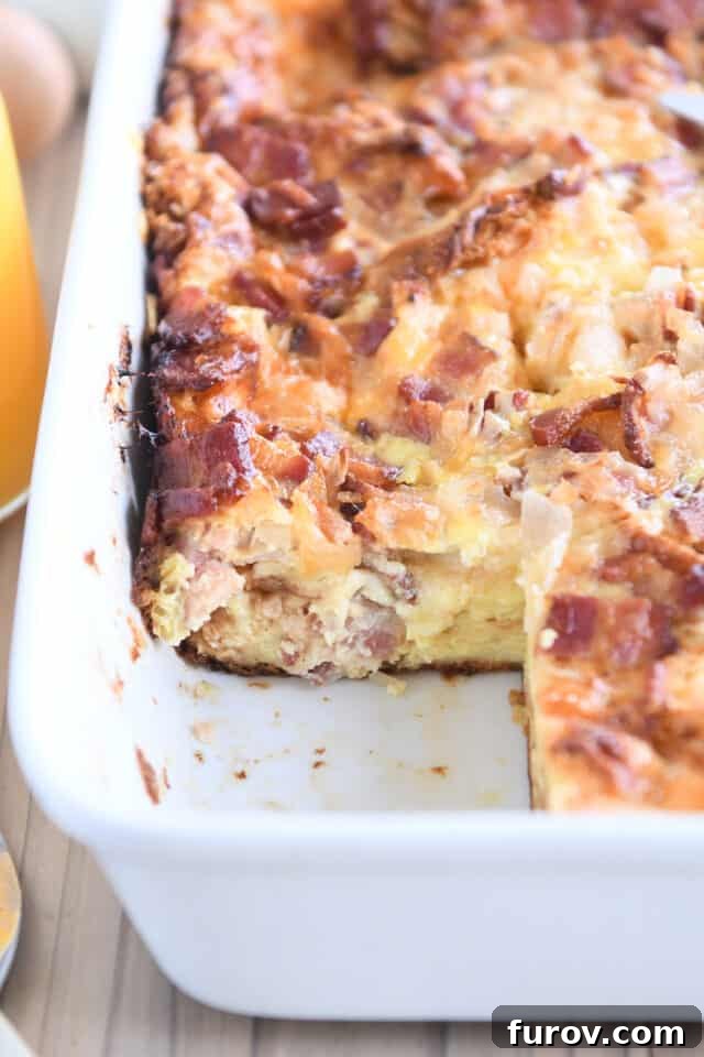 Overnight Croissant Bacon & Cheese Strata 2 Overnight croissant breakfast casserole baked in white 9X13-inch pan with one serving removed, showcasing its golden-brown crust and cheesy interior.