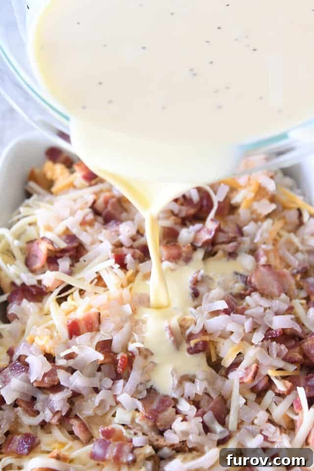 Overnight Croissant Bacon & Cheese Strata 5 Chef pouring creamy egg and milk mixture evenly over the croissant, bacon, and cheese layers in a white 9X13-inch pan, preparing for overnight chilling.