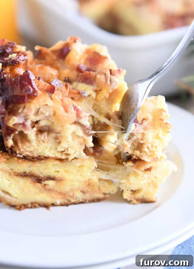 Overnight Croissant Bacon & Cheese Strata 7 A fork taking a delicious bite from the breakfast casserole on a white plate, with long, luscious strings of melted cheese stretching invitingly.