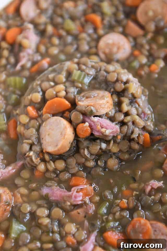 Ladle lifting up scoop of lentil soup with sausage and veggies.