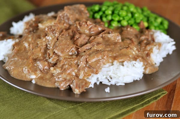 beef stroganoff over a bed of white rice and a scoop of green peas on the side