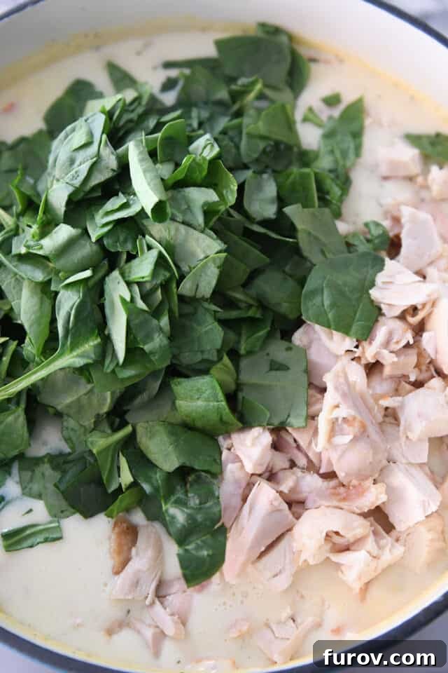 The Ultimate Creamy Chicken Gnocchi Soup 5 Fresh spinach and cooked, chopped chicken are being added to a blue pot filled with creamy chicken gnocchi soup ingredients.