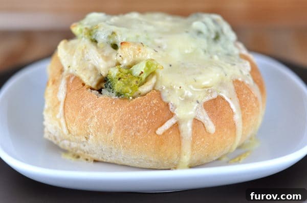 Golden Cordon Bleu Bread Bowls 2 A golden-brown bread bowl on a white plate, overflowing with a creamy mixture of chicken, ham, and vibrant green broccoli, topped with perfectly melted Swiss cheese.