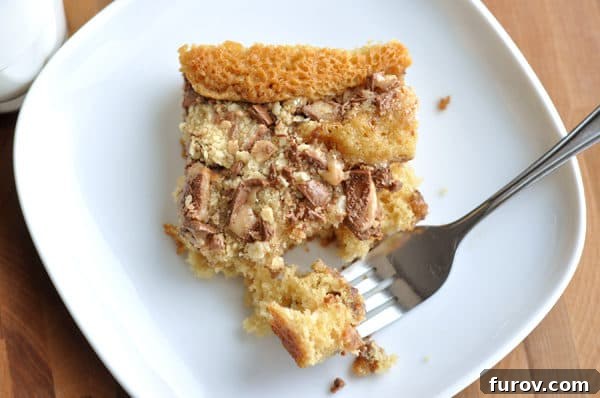 Top view of a piece of Heath Bar cake on a white plate with a bite being taken out with a fork, showing the moist interior and crunchy topping.