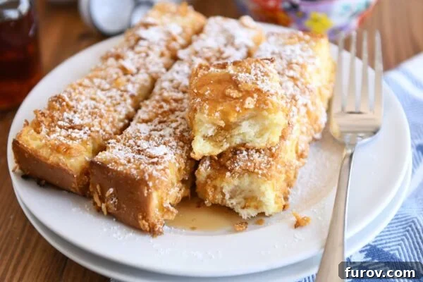 Wake Up to 25+ Festive Holiday Breakfasts 2 Crunchy baked french toast sticks on white plate with powdered sugar and syrup.