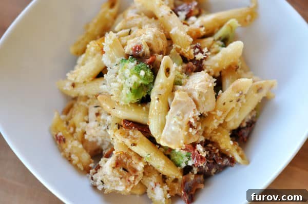 Hearty Chicken and Broccoli Penne Bake with Smoked Mozzarella 10 Top-down view of a white casserole dish generously filled with baked penne pasta, succulent chicken pieces, vibrant broccoli florets, rich melted cheese, and sun-dried tomatoes.
