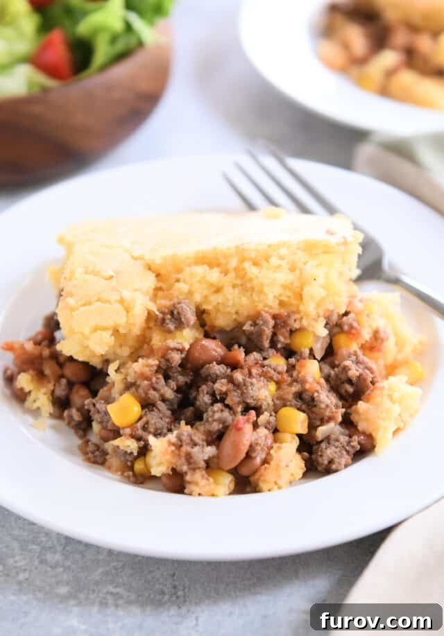 Cornbread topped beef, bean, and corn mixture on white plate with fork.