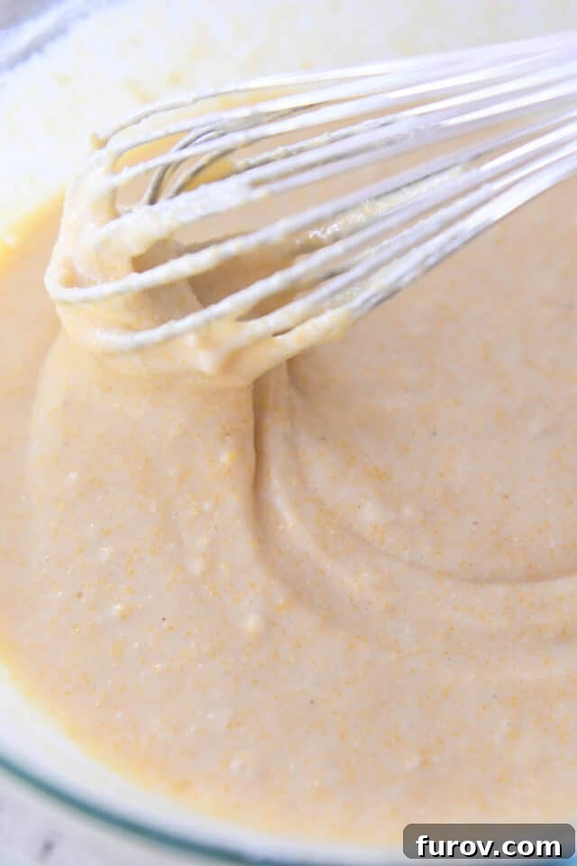 Whisk stirring cornbread batter in glass bowl.