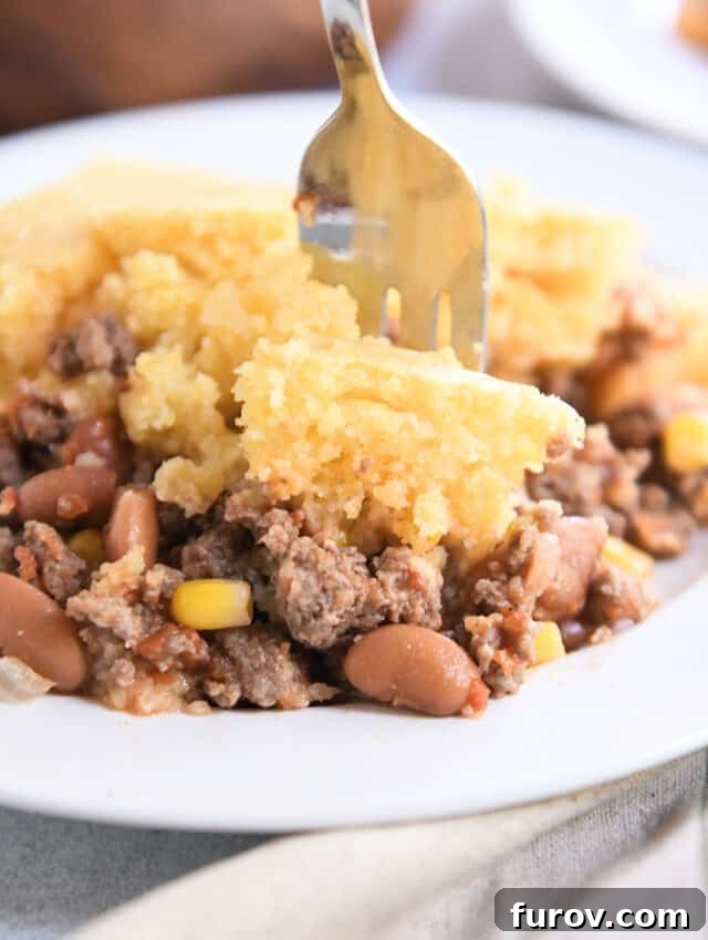 Fork taking bite of cornbread topped beef and bean casserole.