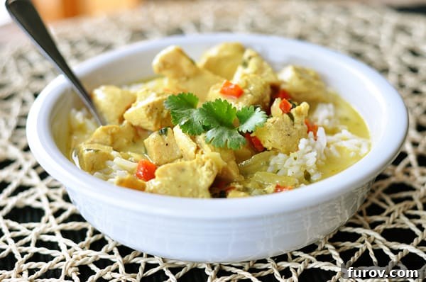 Close-up shot of a white bowl with chicken curry soup over a bed of white rice, ready to be enjoyed.