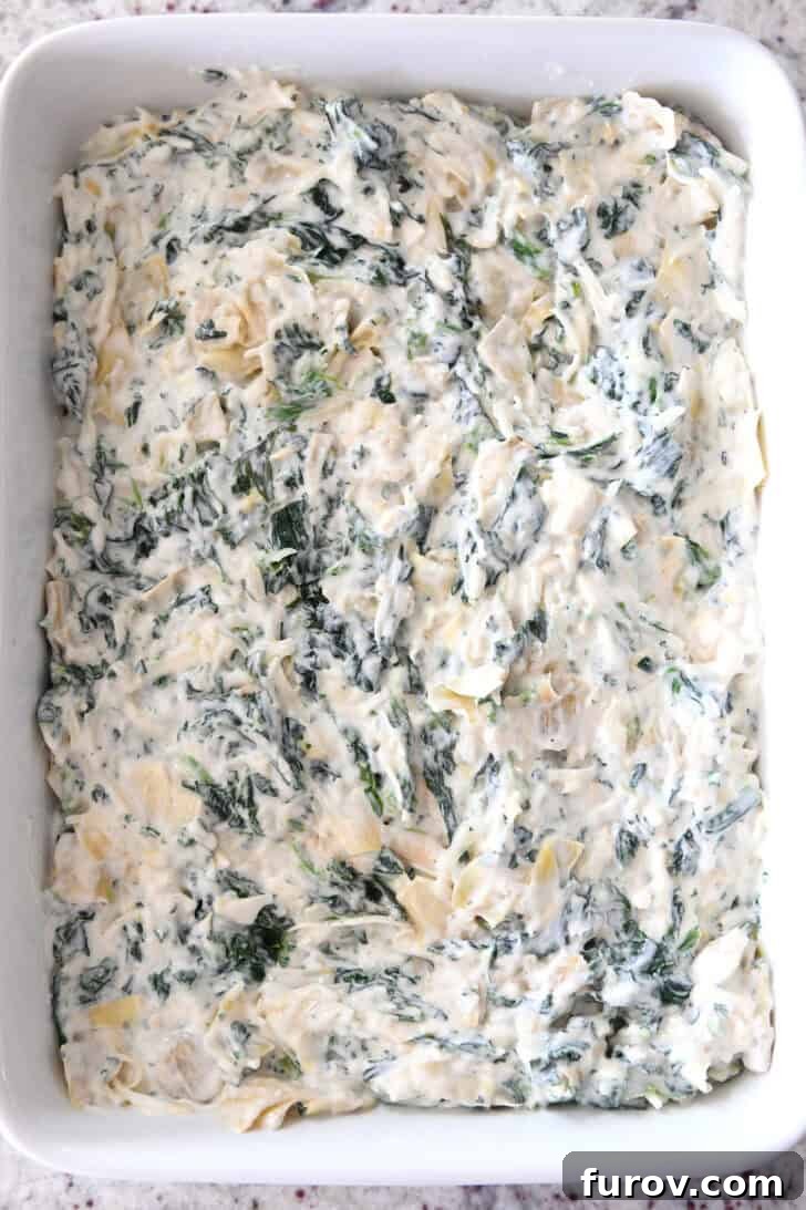 Ultimate Creamy Spinach Artichoke Dip 5 Top down view of a white casserole dish with uncooked creamy spinach artichoke dip, ready for the oven.