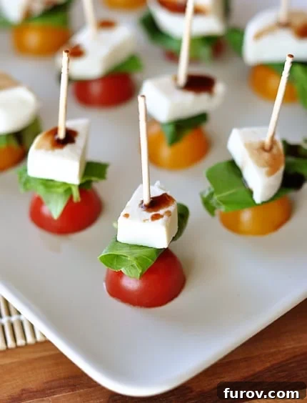 White platter with toothpick Caprese skewers, garnished with fresh basil leaves.