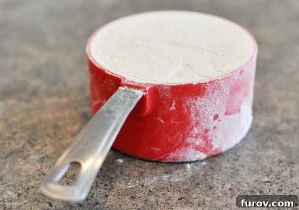 A red measuring cup full of white flour, illustrating a standard volume measurement.