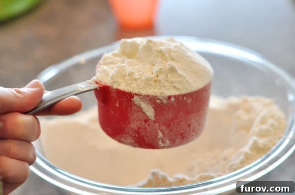A red measuring cup overfilled with white flour, demonstrating the piled high flour before leveling.