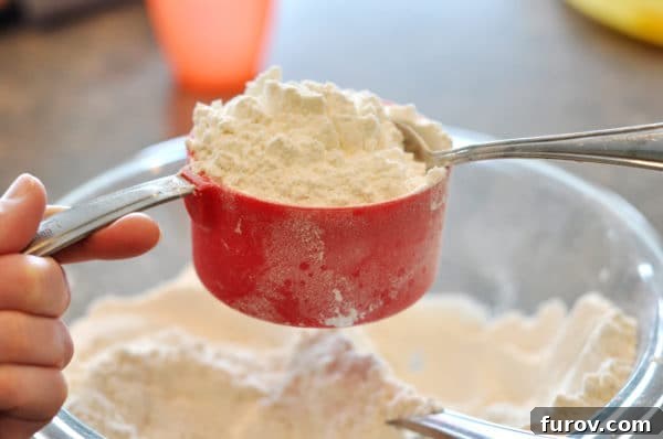 A spoon scooping white flour into a red measuring cup, illustrating the spoon and sweep technique.