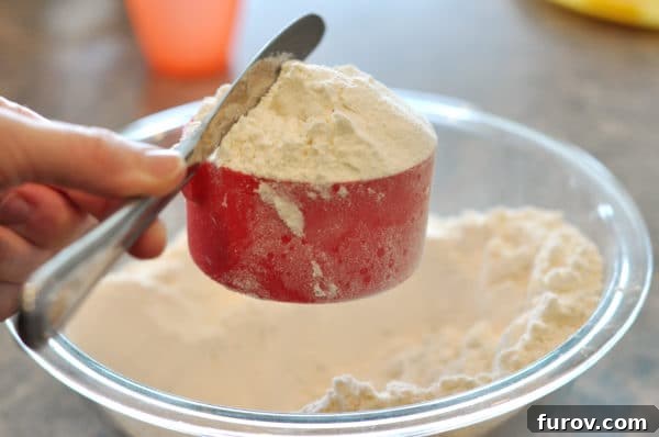 A butter knife leveling off flour in a red measuring cup, completing the spoon and sweep method.