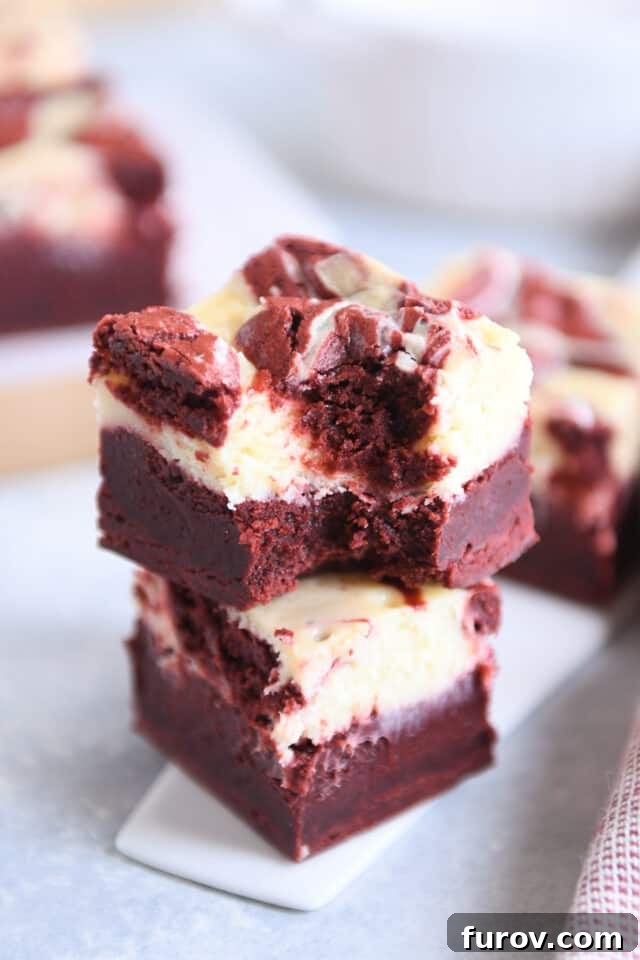 Two red velvet cheesecake brownies stacked with bite taken out of the top brownie.