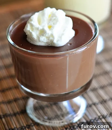 A glass dish with creamy, rich homemade chocolate pudding topped generously with fluffy whipped cream, inviting a delicious spoonful.