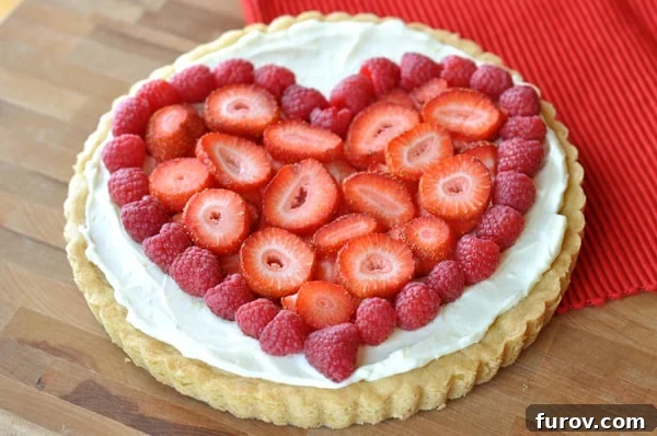 A sugar cookie crust with vanilla frosting and strawberries and raspberries on top in the shape of a heart, ideal for Valentine's Day.