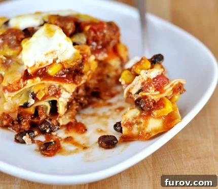 White plate with red sauce Mexican lasagna filled with beef, black beans, and corn.
