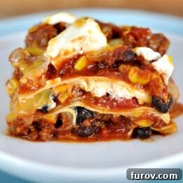 A slice of Mexican lasagna on a white plate, showcasing layers of noodles, beef, beans, corn, and cheese.