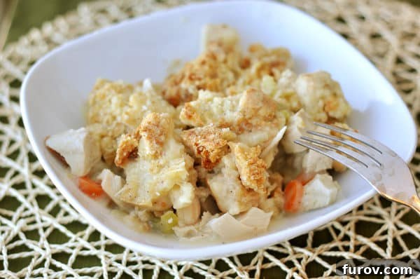 White plate with a generous serving of creamy chicken pot pie filling and a golden brown Parmesan crumble top, garnished with fresh herbs.