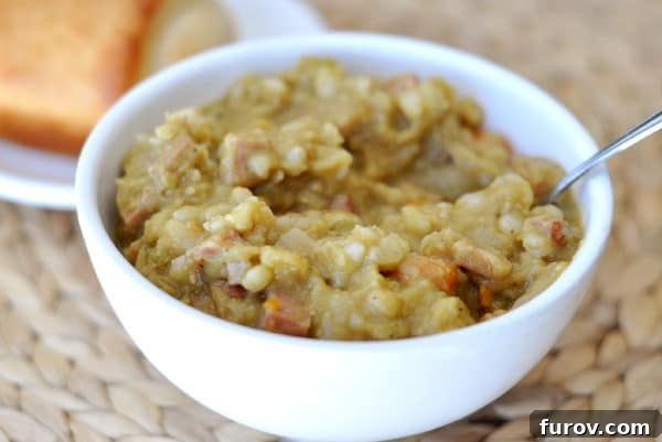 A comforting white bowl filled with thick slow cooker split pea and ham soup, garnished with fresh herbs.