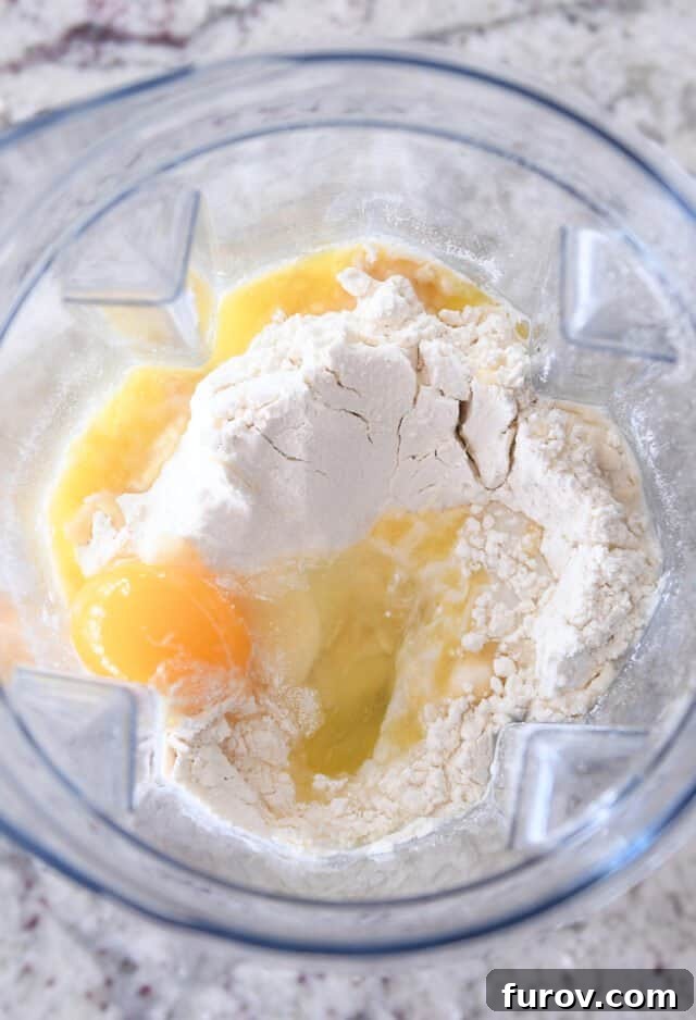Top-down view of a blender filled with Swedish pancake batter ingredients: flour, eggs, milk, and melted butter, ready for blending.