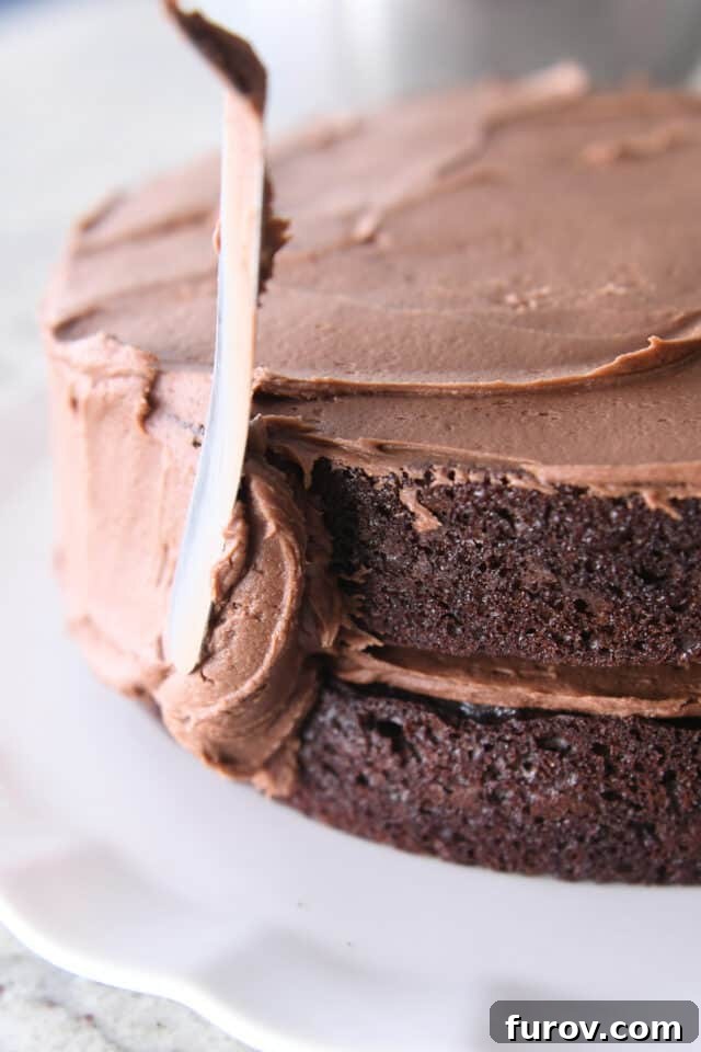 An offset spatula expertly spreads rich chocolate frosting over a freshly baked chocolate cake, preparing it for its final presentation.