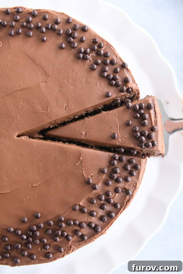A top-down view of a frosted chocolate cake with a slice removed, revealing its rich, dark interior and ready for serving.