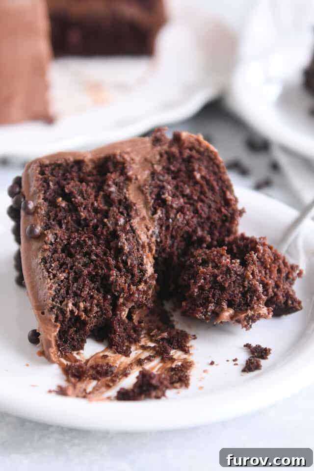 A delectable slice of chocolate cake with creamy chocolate frosting sits on a white plate, accompanied by a fork, inviting a delightful indulgence.