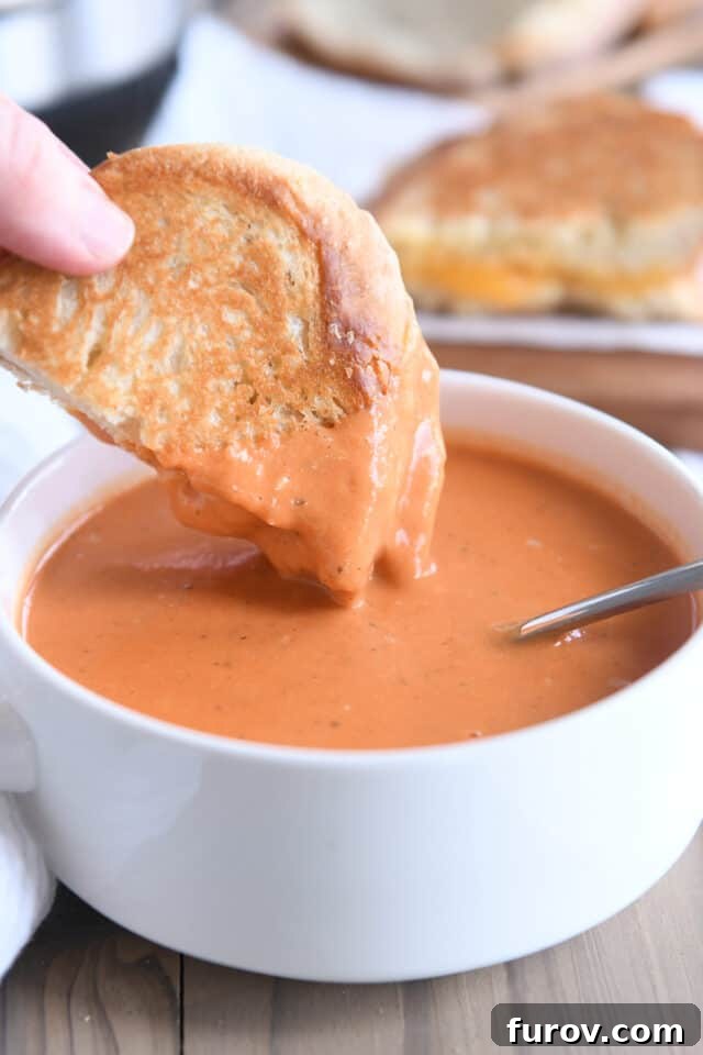 A slice of grilled cheese on sourdough bread being dipped into a bowl of creamy Instant Pot tomato basil soup, highlighting the perfect comfort food pairing.