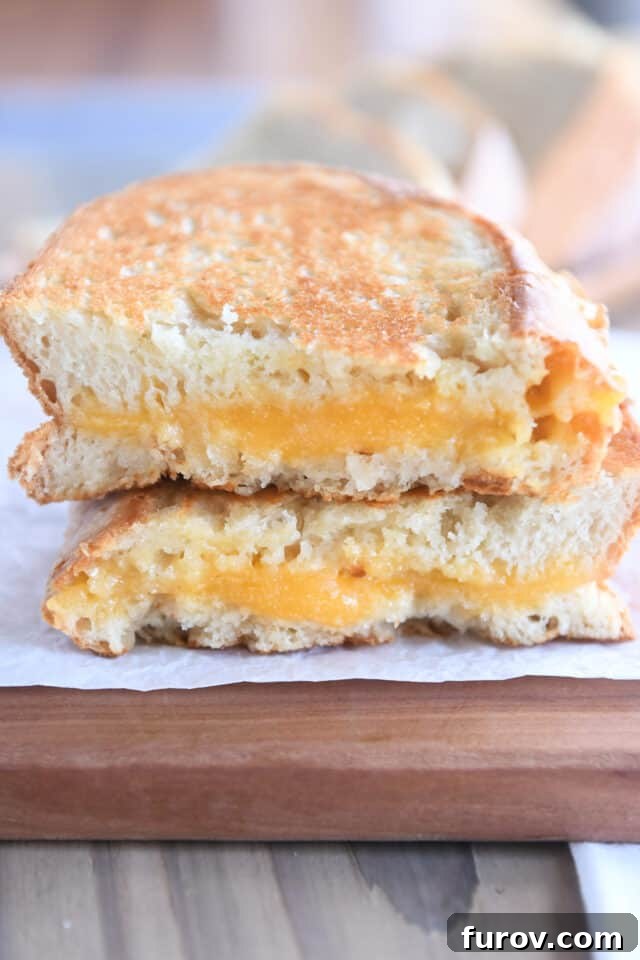 Two half slices of grilled cheese sandwich on wood cutting board.