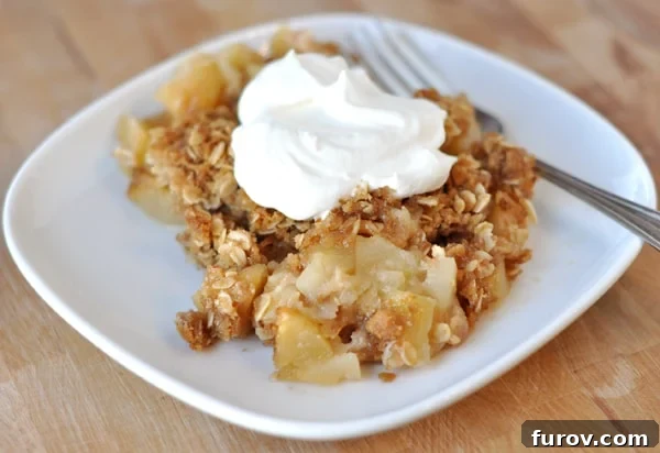 A white plate with a baked apple crisp, elegantly topped with a generous swirl of whipped cream, ready to be enjoyed.