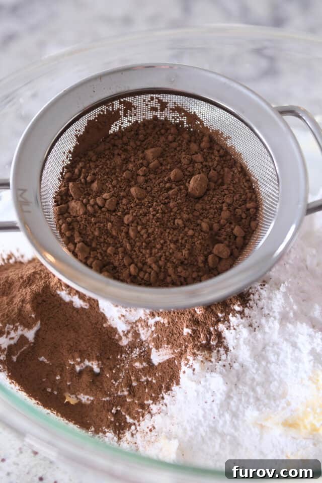 Sifting cocoa powder into glass bowl with powdered sugar and butter.