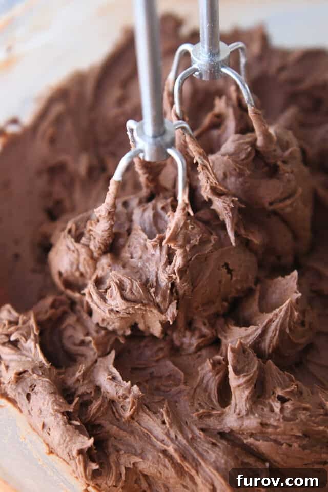 Mixing chocolate buttercream frosting in glass bowl with mixer.