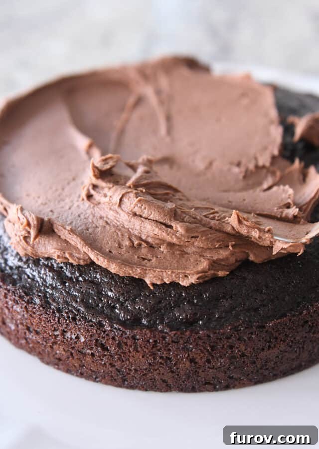 Spreading chocolate frosting on top of one round of chocolate cake.