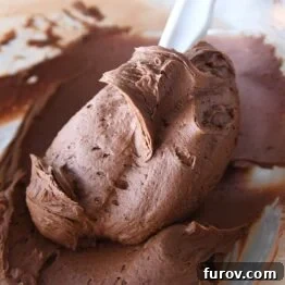 rubber spatula swirling chocolate frosting in glass bowl