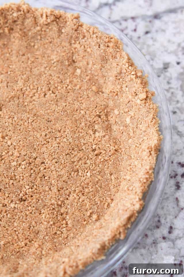 Crisp, Buttery Graham Cracker Crust 8 Half view of a golden brown, perfectly baked graham cracker crust cooling in a glass pie plate, showcasing its pristine form.